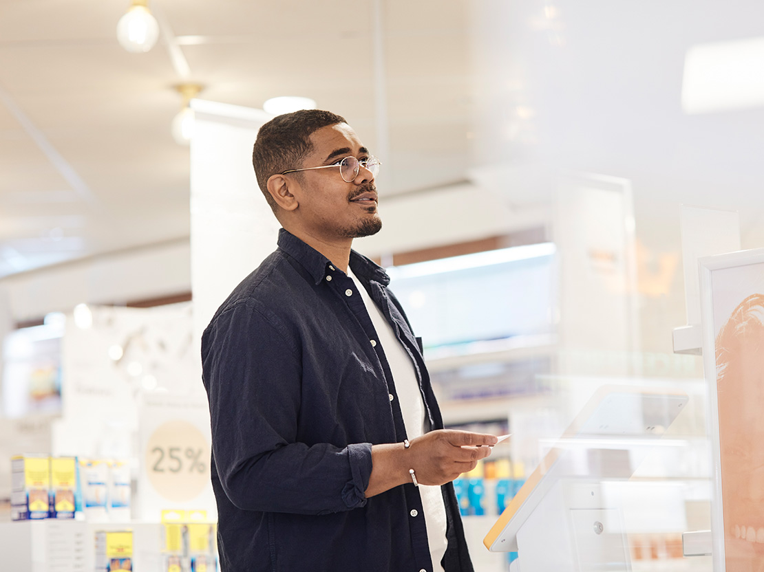 Man i glasögon står och väntar med kölapp på apotek
