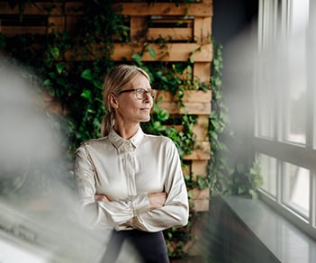 Kvinna på kontor i vit blus blickar ut genom fönstret