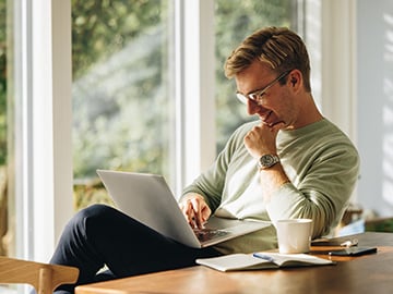 Man sitter vid fönster med laptop