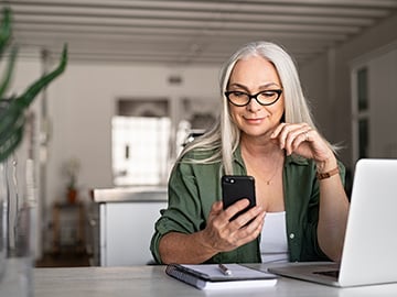 Kvinna vid dator som tittar på sin smartphone