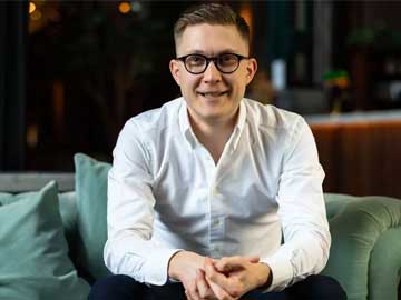 Anders Nordkvist sittandes i grön soffa med stort leende